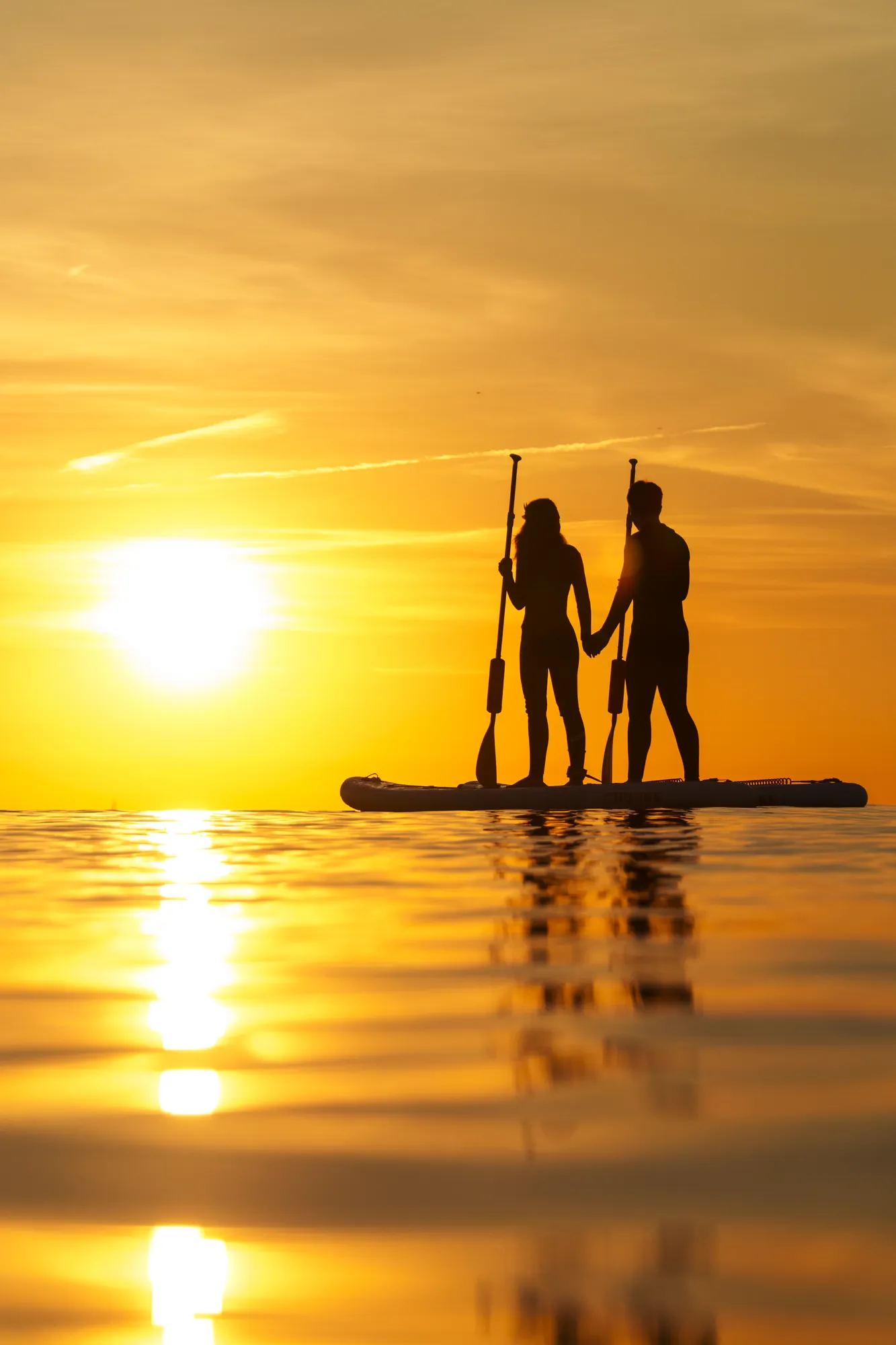 Couple paddle boarding at sunset in Sitges, golden light towards Terramar
