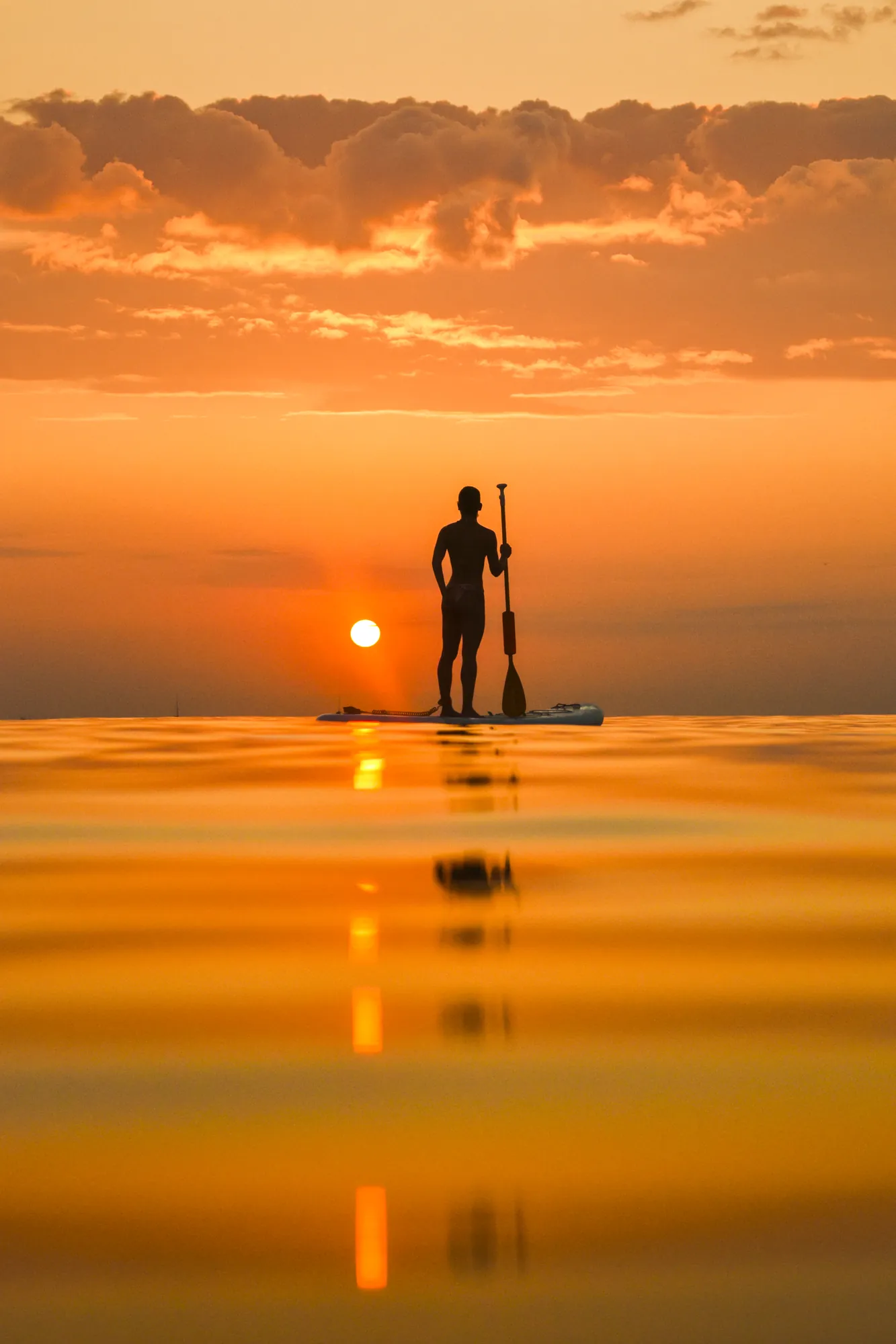 Man stand up paddle boarding at sunrise at Platja de la Riera Xica, Sitges, calm open sea